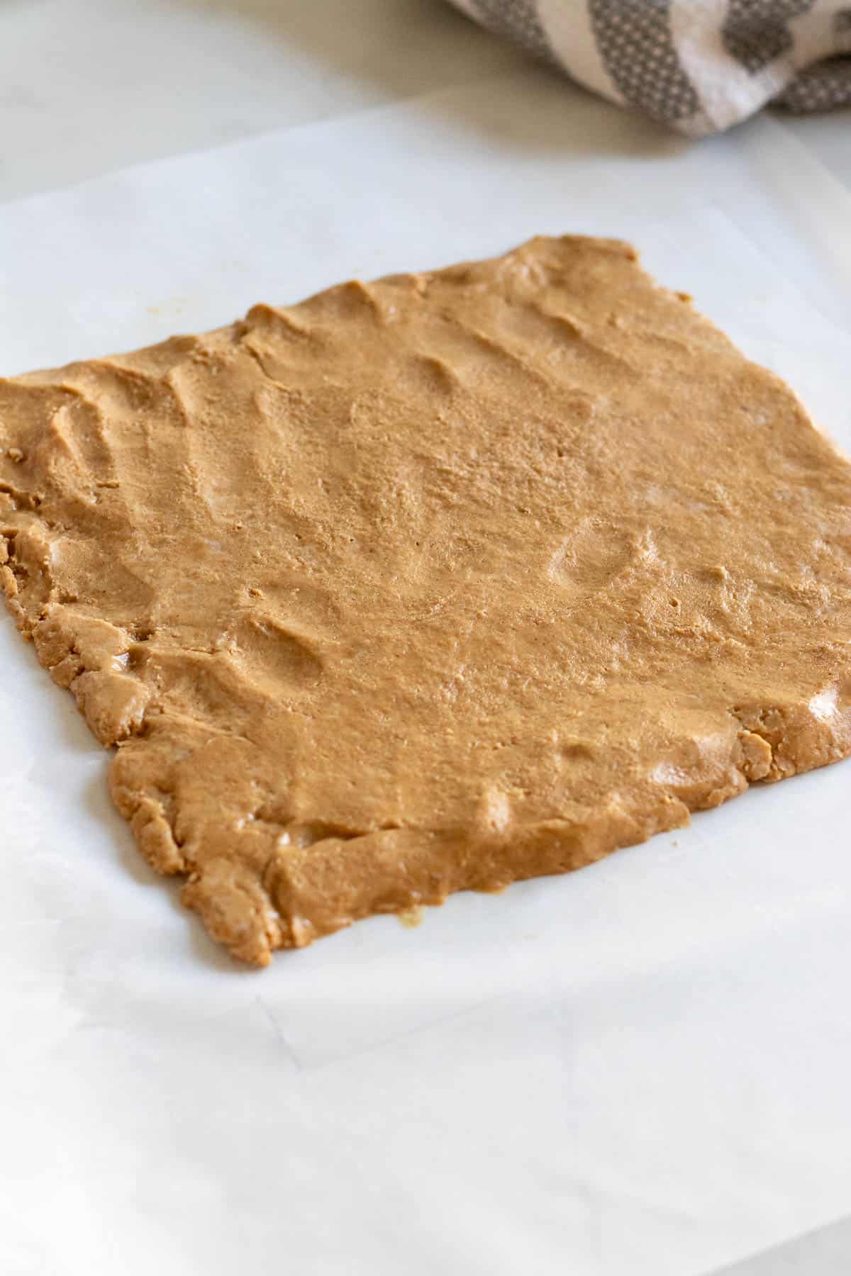 peanut butter filling rolled out into a square sitting on parchment