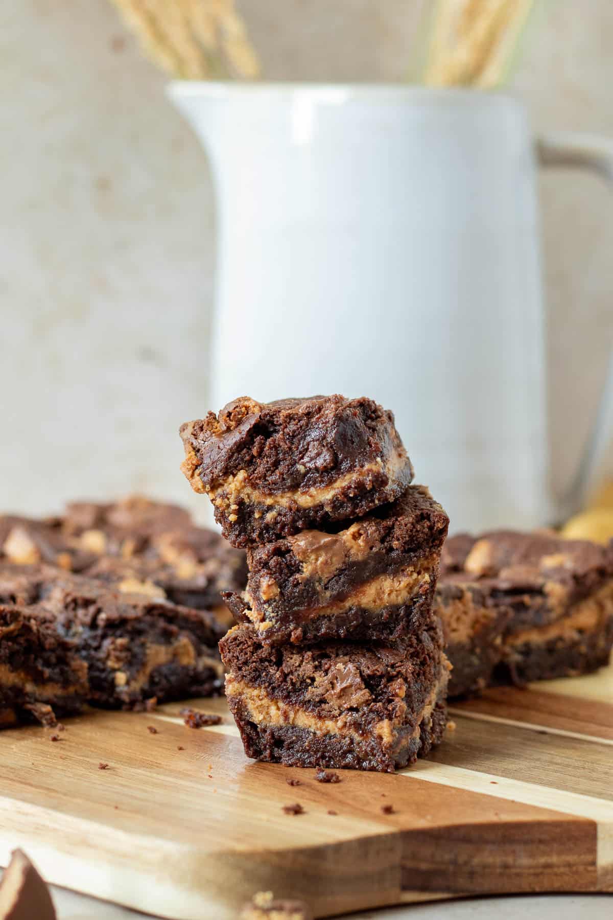 stack of chocolate peanut butter cup brownies on a wood cutting board with a white picture in the background