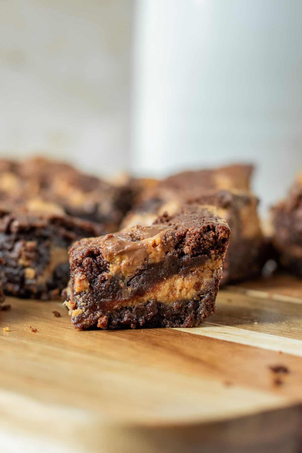 close up of a brownie with a peanut butter layer and peanut butter cups sitting on a wood board