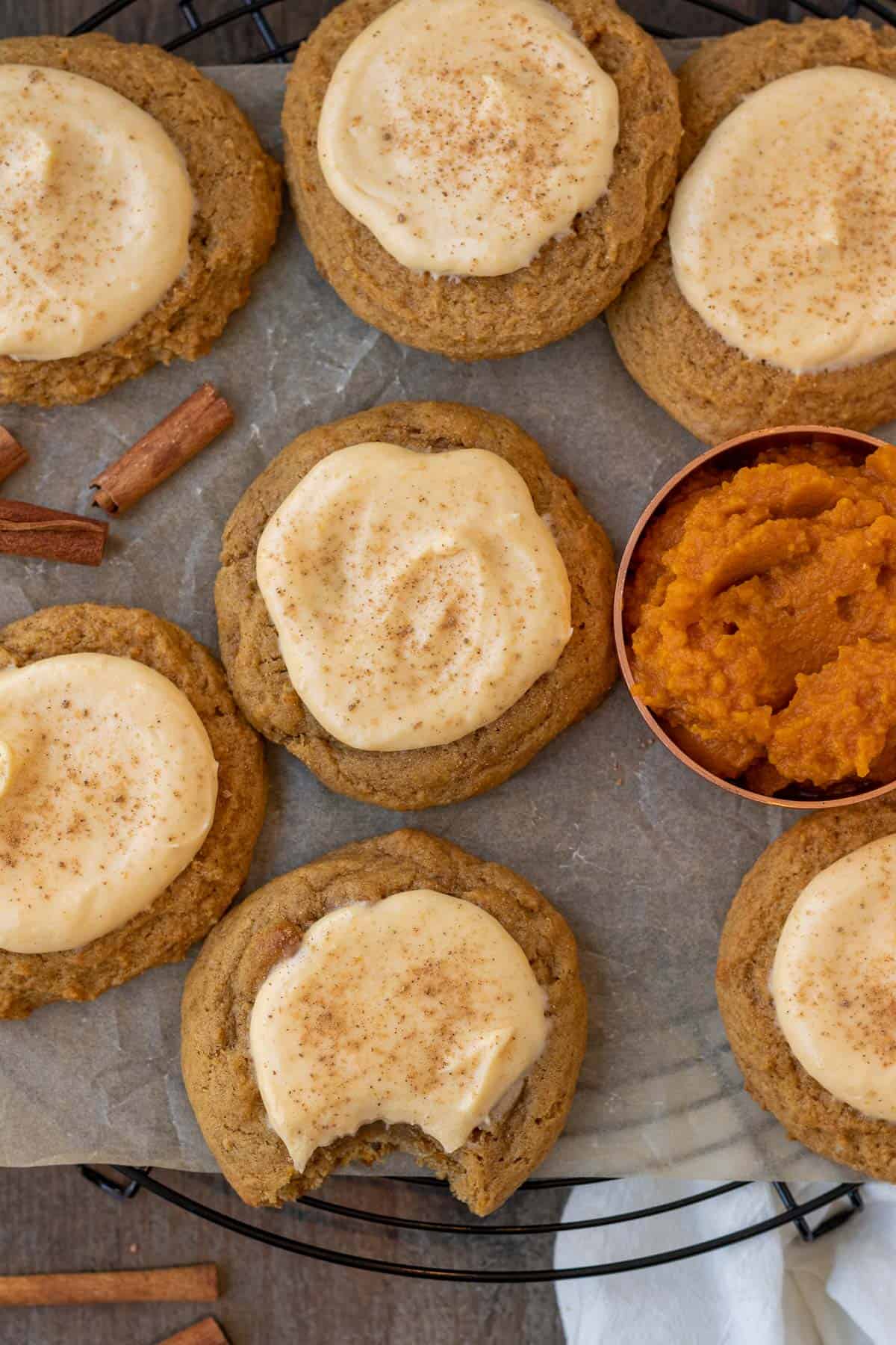 pumpkin cheesecake cookies on a cooling rack on a wood background with pumpkin puree in a measuring cup