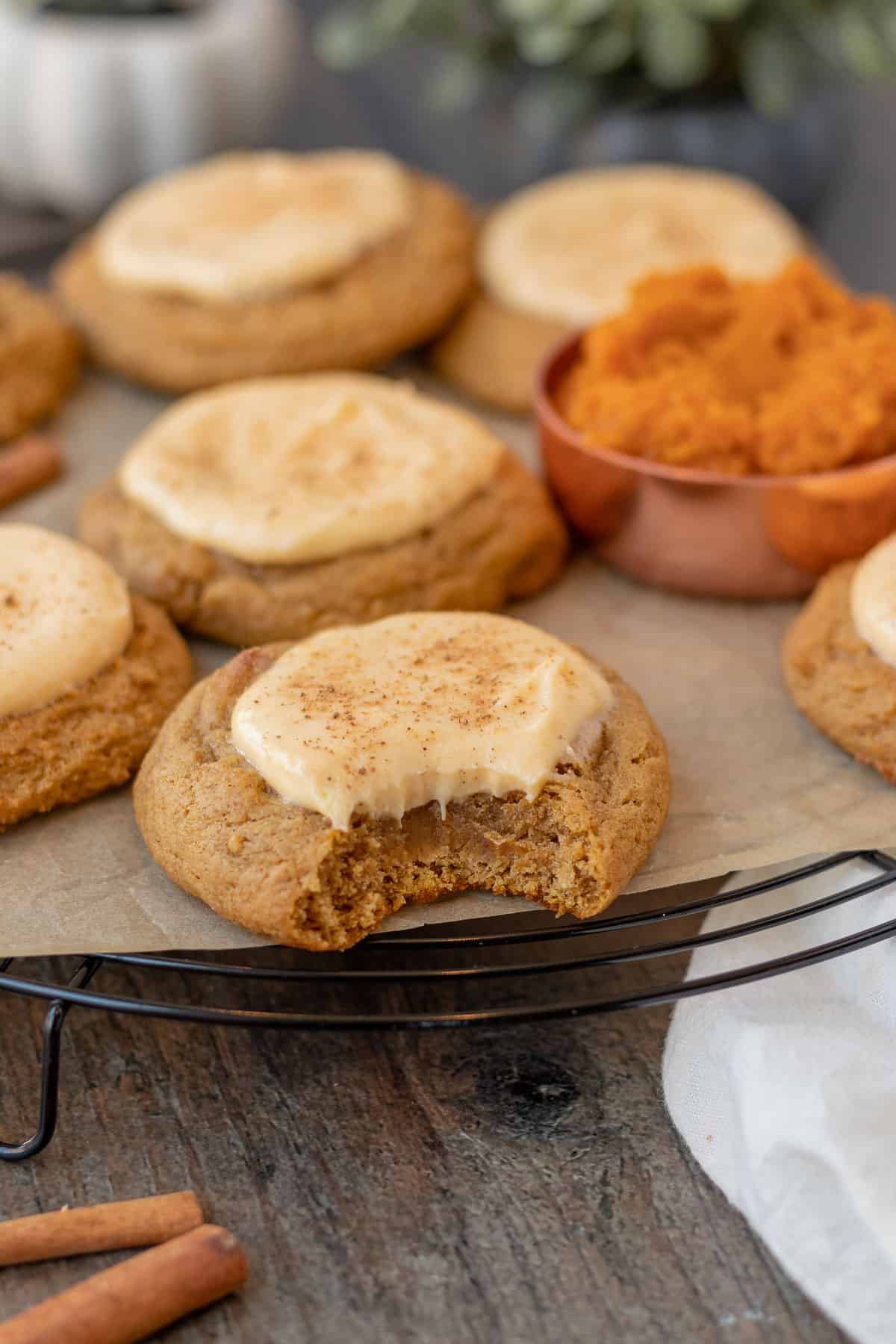 pumpkin cheesecake cookies sitting on a black wire cooling rack with measuring cup of pumpkin next to them