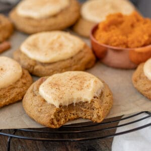 pumpkin cheesecake cookies sitting on a black wire cooling rack with measuring cup of pumpkin next to them