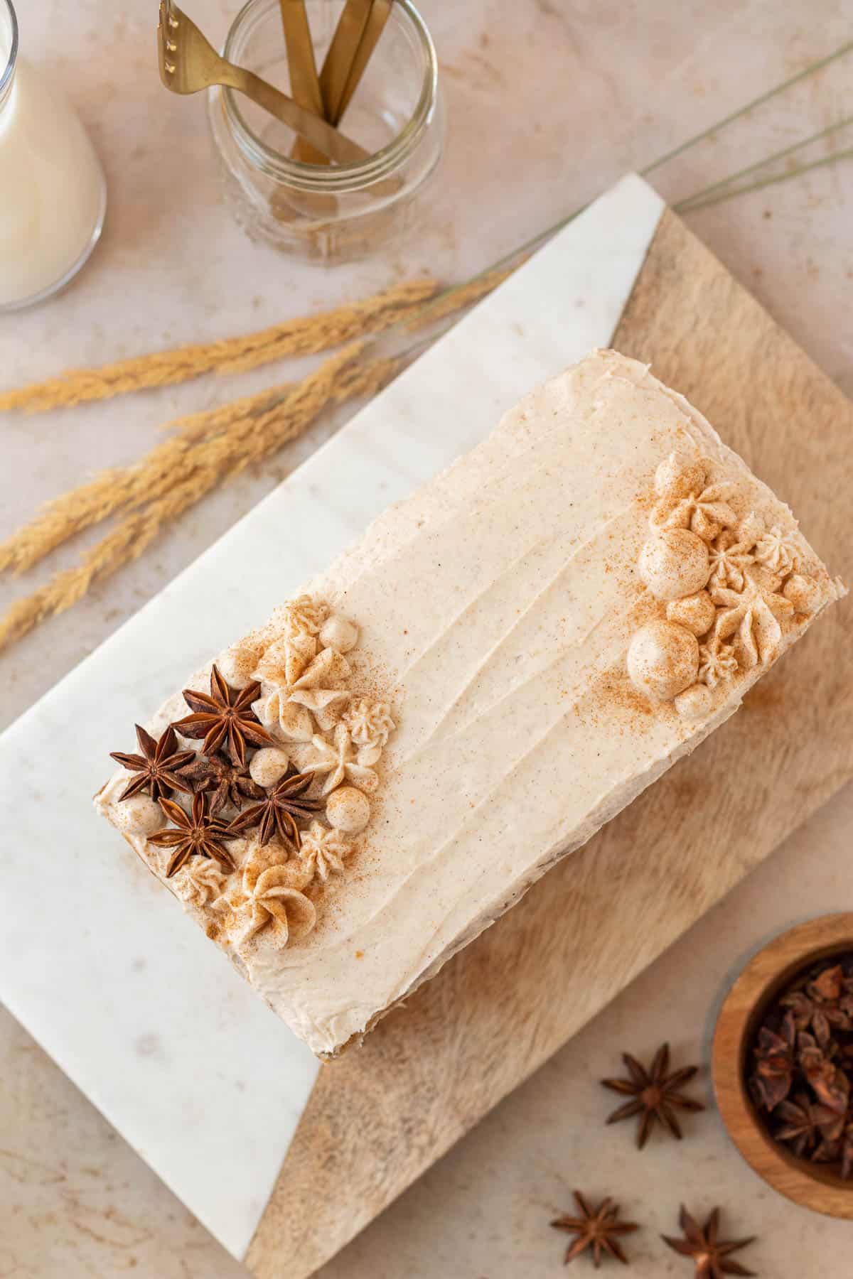 a rectangular chai cake decorated with rosettes of frosting and star anise pods sitting on a wood and marble cutting board