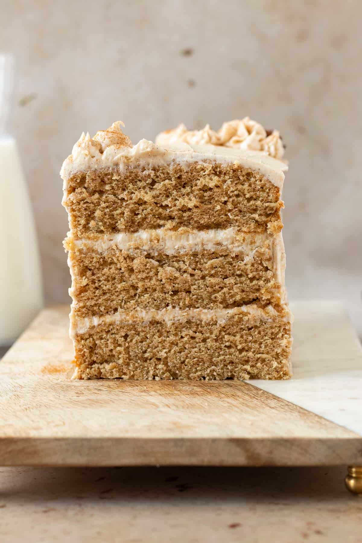 chai cake sliced open showing 3 layers of cake and 2 layers of frosting, sitting on a wood cutting board