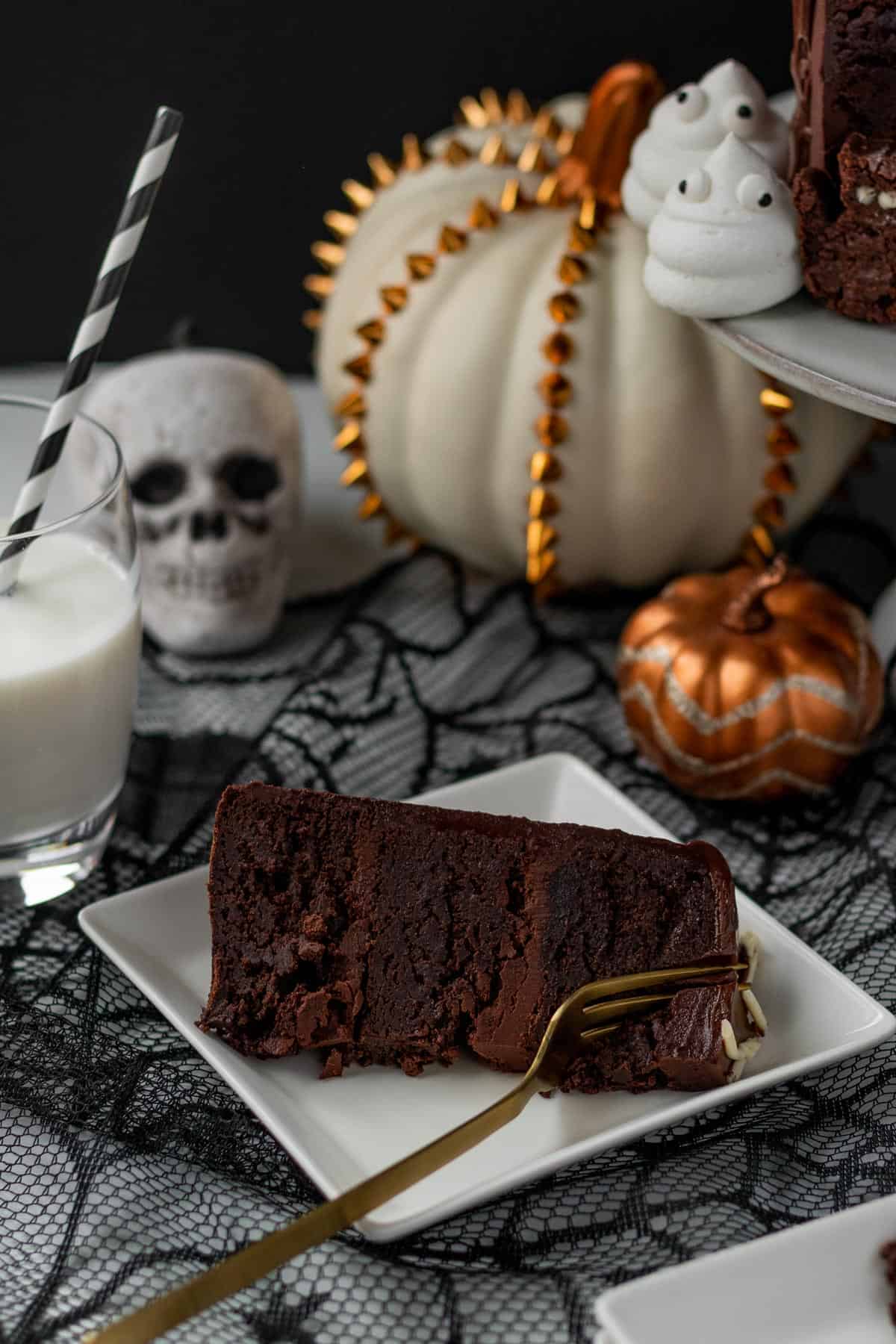 slice of chocolate brownie cake on a square white plate on top of a spider web table runner