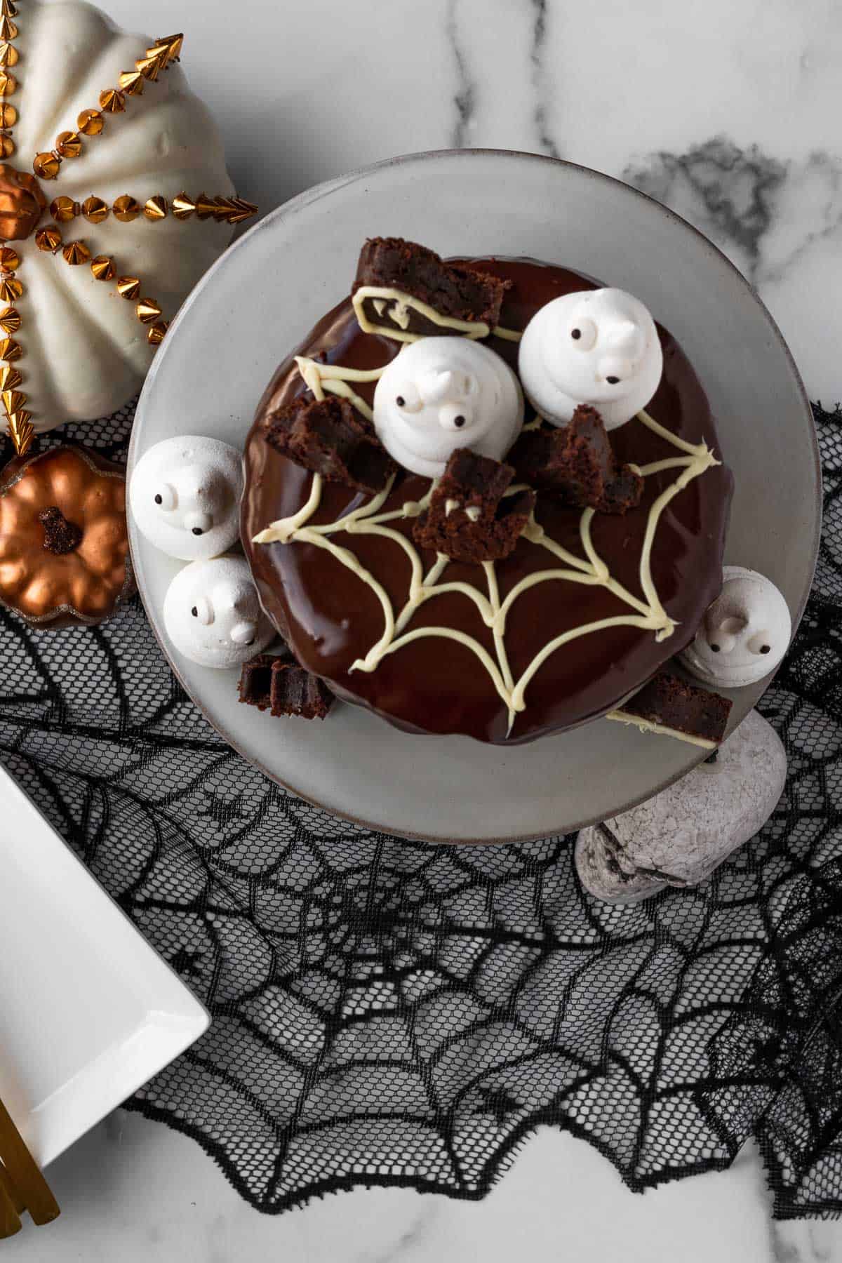 top view of a chocolate cake with a white spider web and meringue ghosts