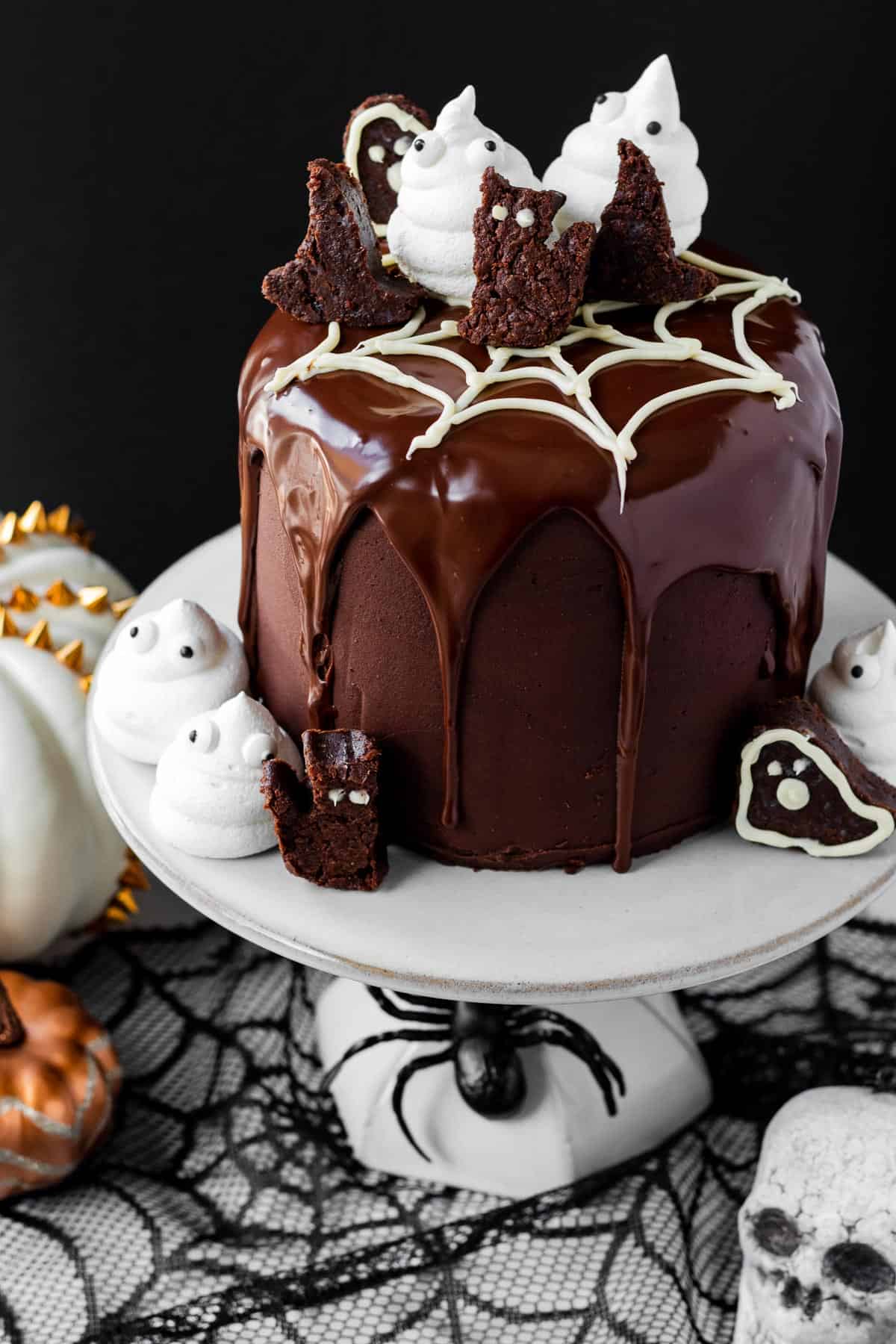 chocolate brownie cake decorated with meringue ghosts, halloween brownies sitting on white cake stand with halloween decor