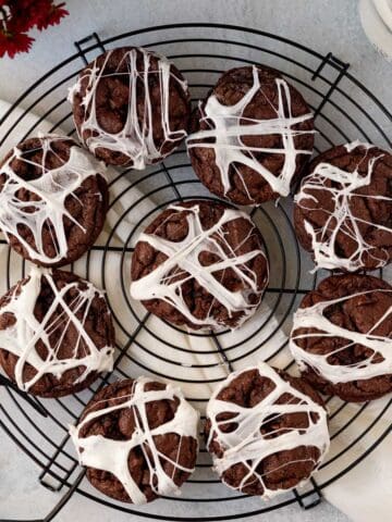 double chocolate chip cookies with marshmallow spider webs sitting on a black round cooling rack