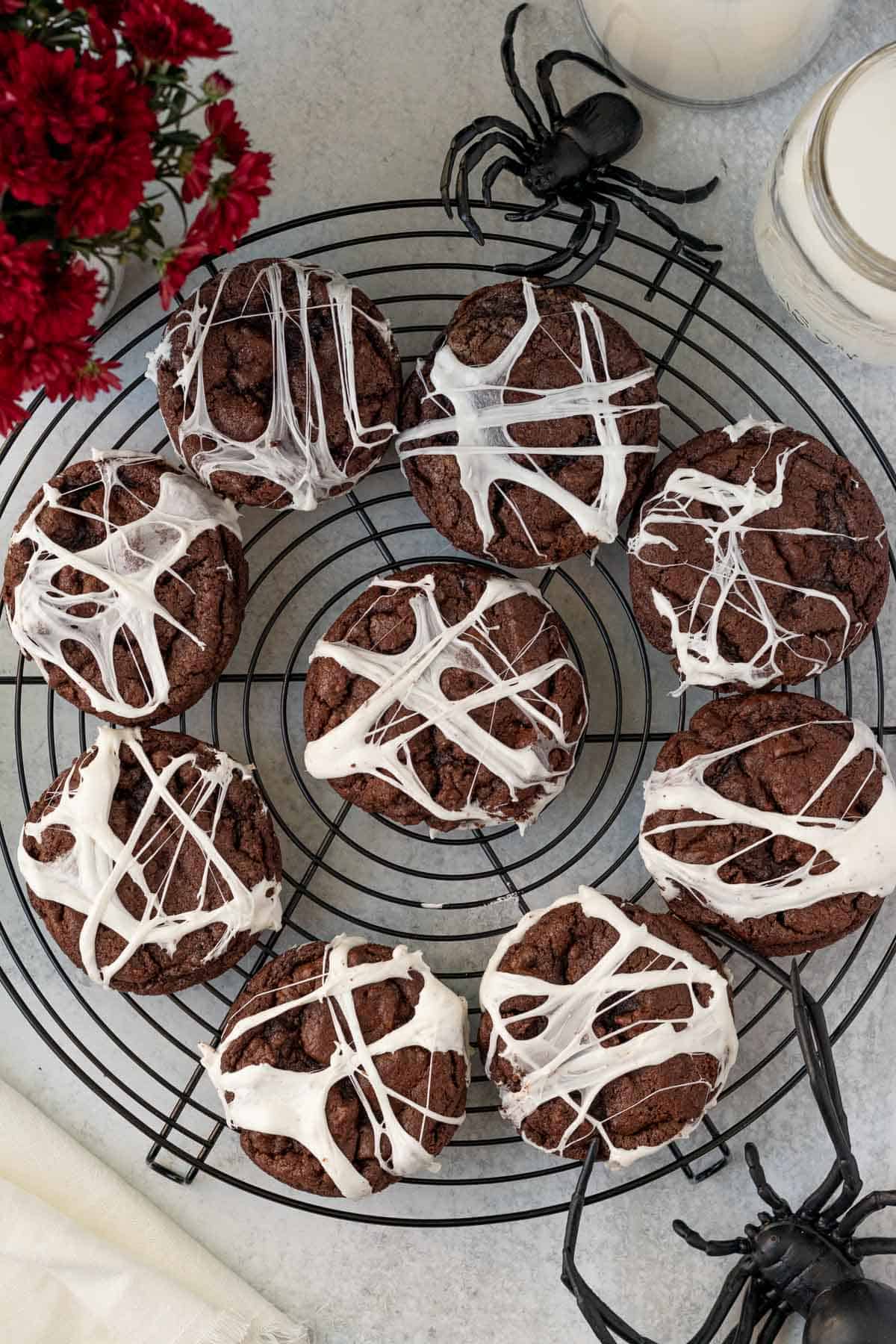 chocolate cookies with marshmallow spider webs sitting on top of a black circular cooling rack