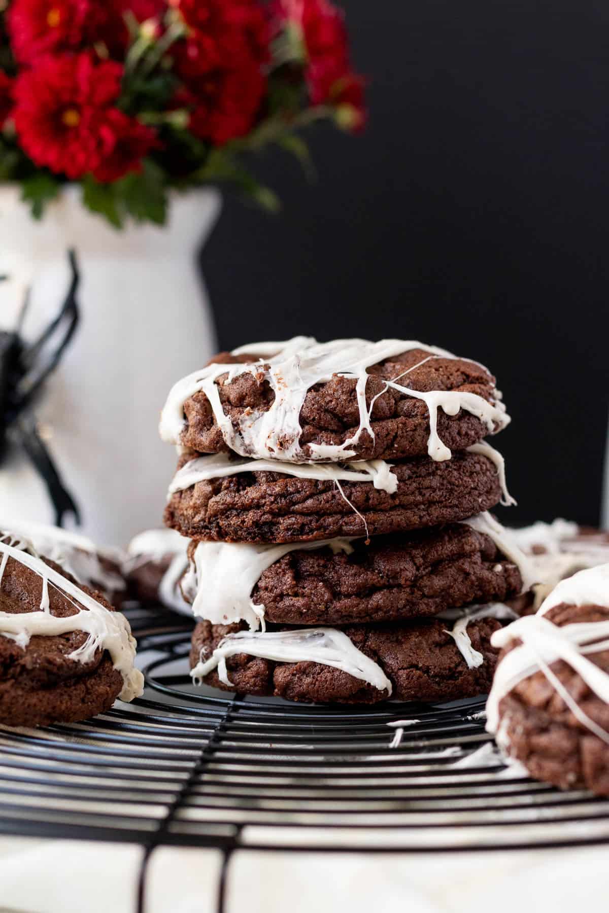 stack of spider web cookies sitting on a cooling rack with a white vase with a fake black spider in the background