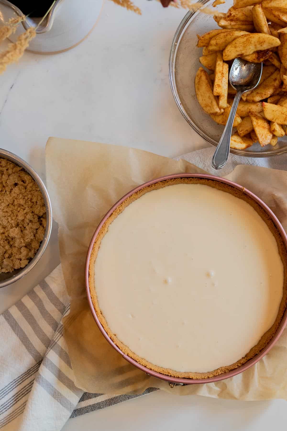 unbaked brown sugar cheesecake with bowl of sliced apples and bowl of crumble topping