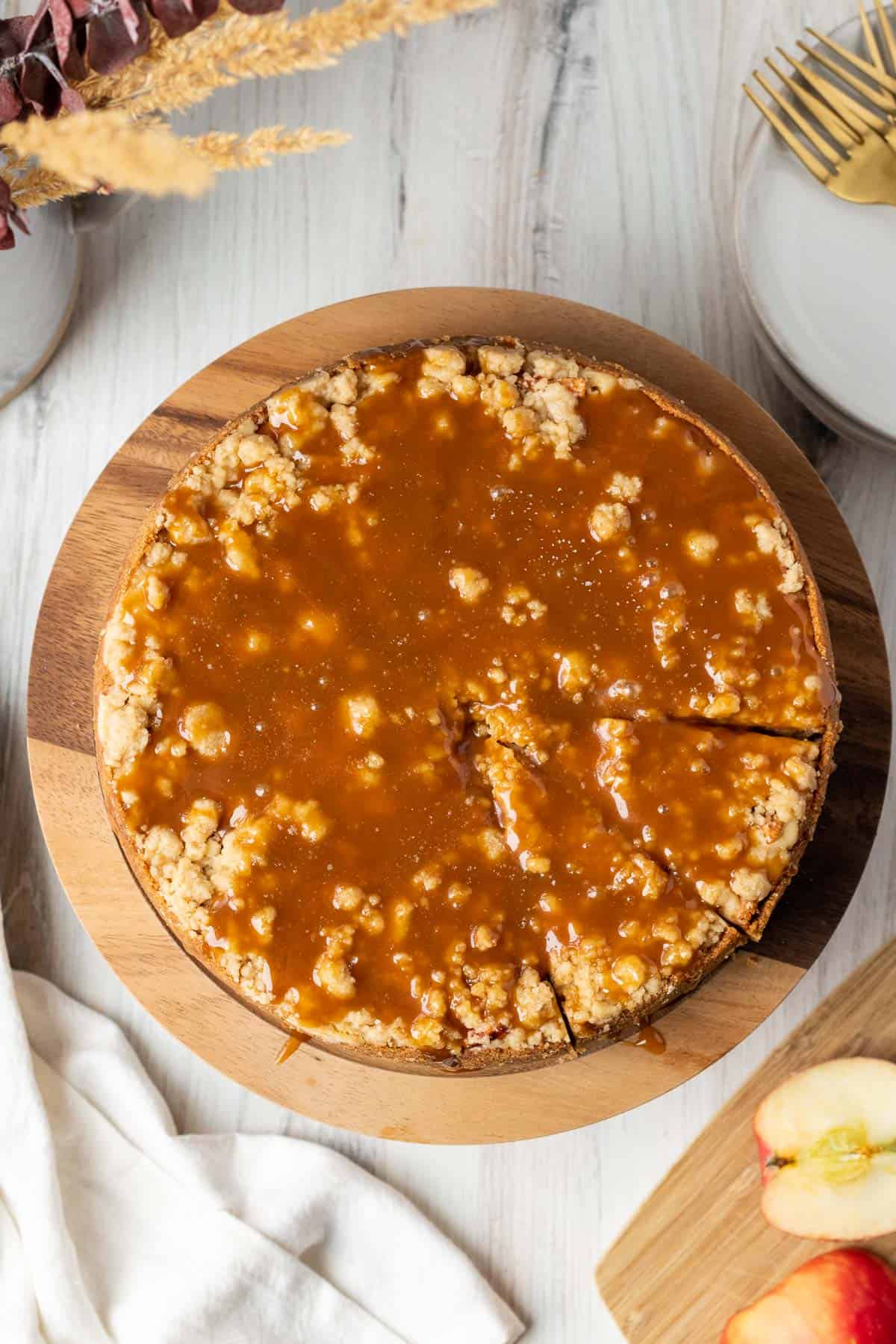 apple crumble cheesecake with salted caramel on top on a wooden cake stand