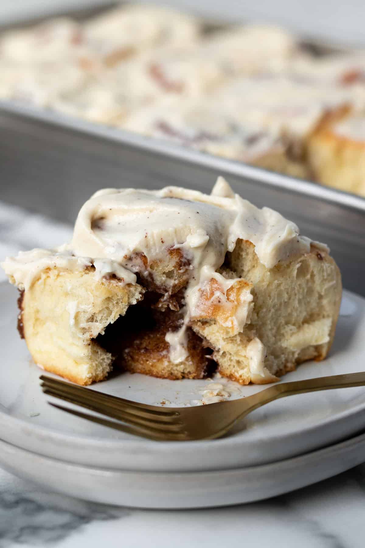 close up of a brioche cinnamon roll cut open sitting on a plate with a gold fork