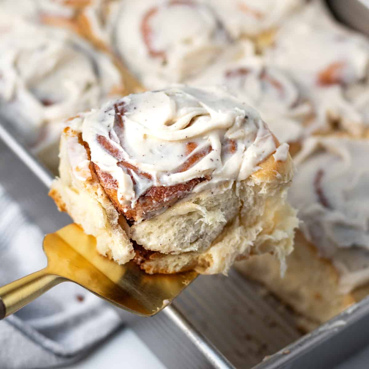 gold spatula lifting a brioche cinnamon roll out of a pan