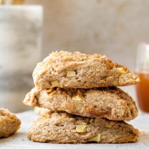 stack of apple scones on a parchment lined wooden cutting board with a marble utensil holder in the background