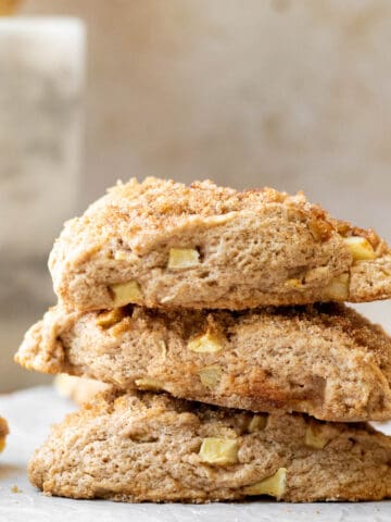 stack of apple scones on a parchment lined wooden cutting board with a marble utensil holder in the background