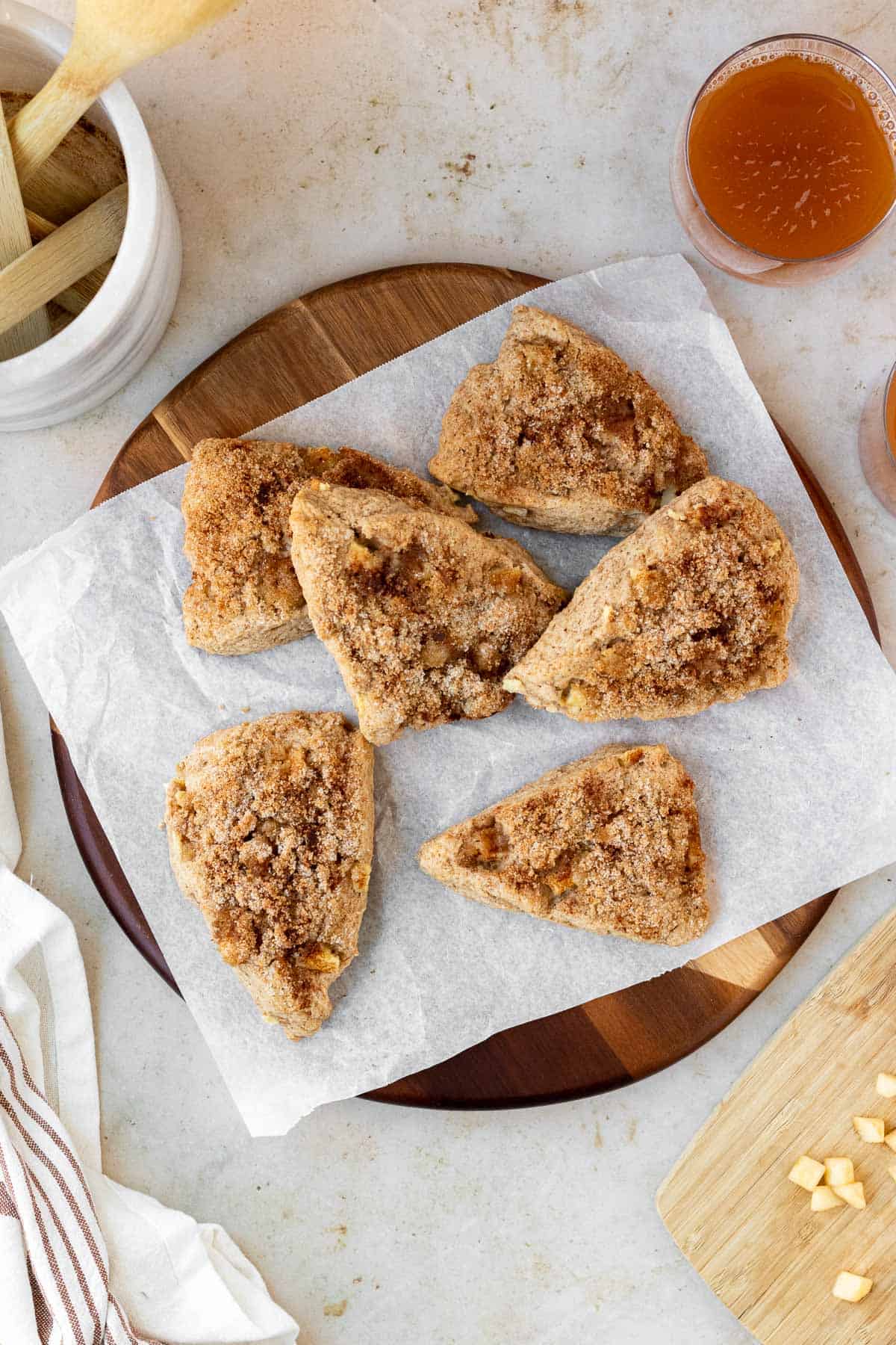apple cinnamon scones sit atop a parchment lined round wood cutting board