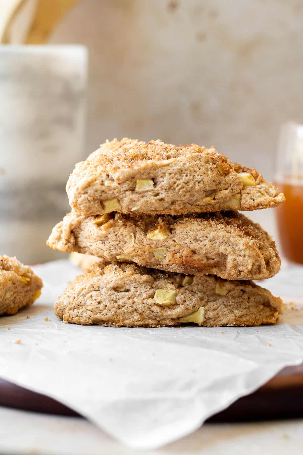 stack of apple scones on a parchment lined wooden cutting board with a marble utensil holder in the background