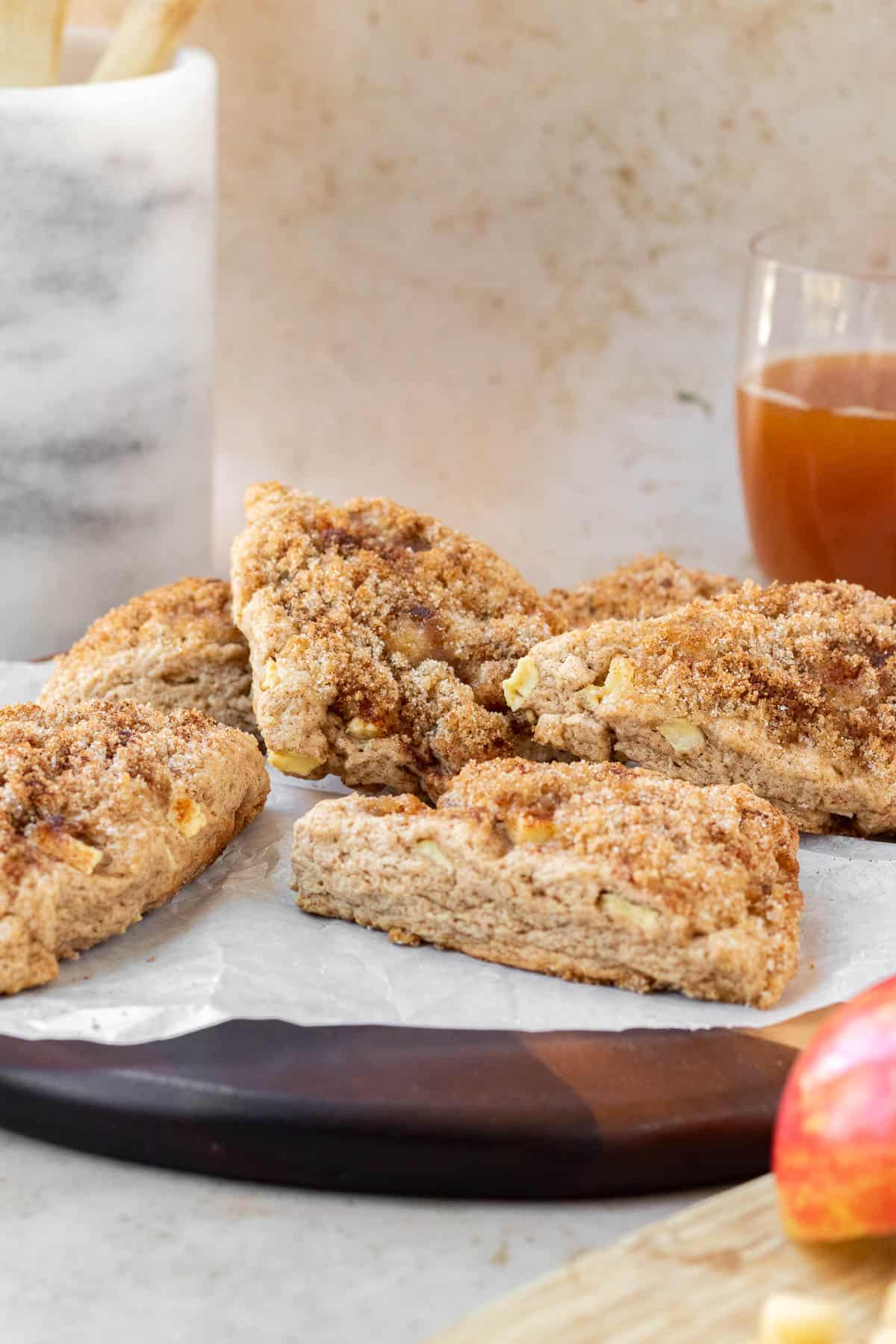 apple cinnamon scones on a wooden cutting board with a glass of apple cider in the background