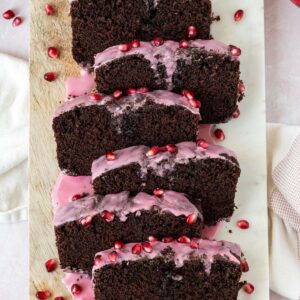 chocolate loaf cake topped with a pomegranate glaze and sliced on top of a wood and marble cutting board