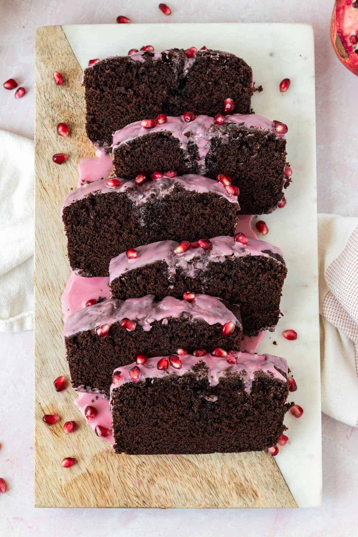 chocolate loaf cake topped with a pomegranate glaze and sliced on top of a wood and marble cutting board