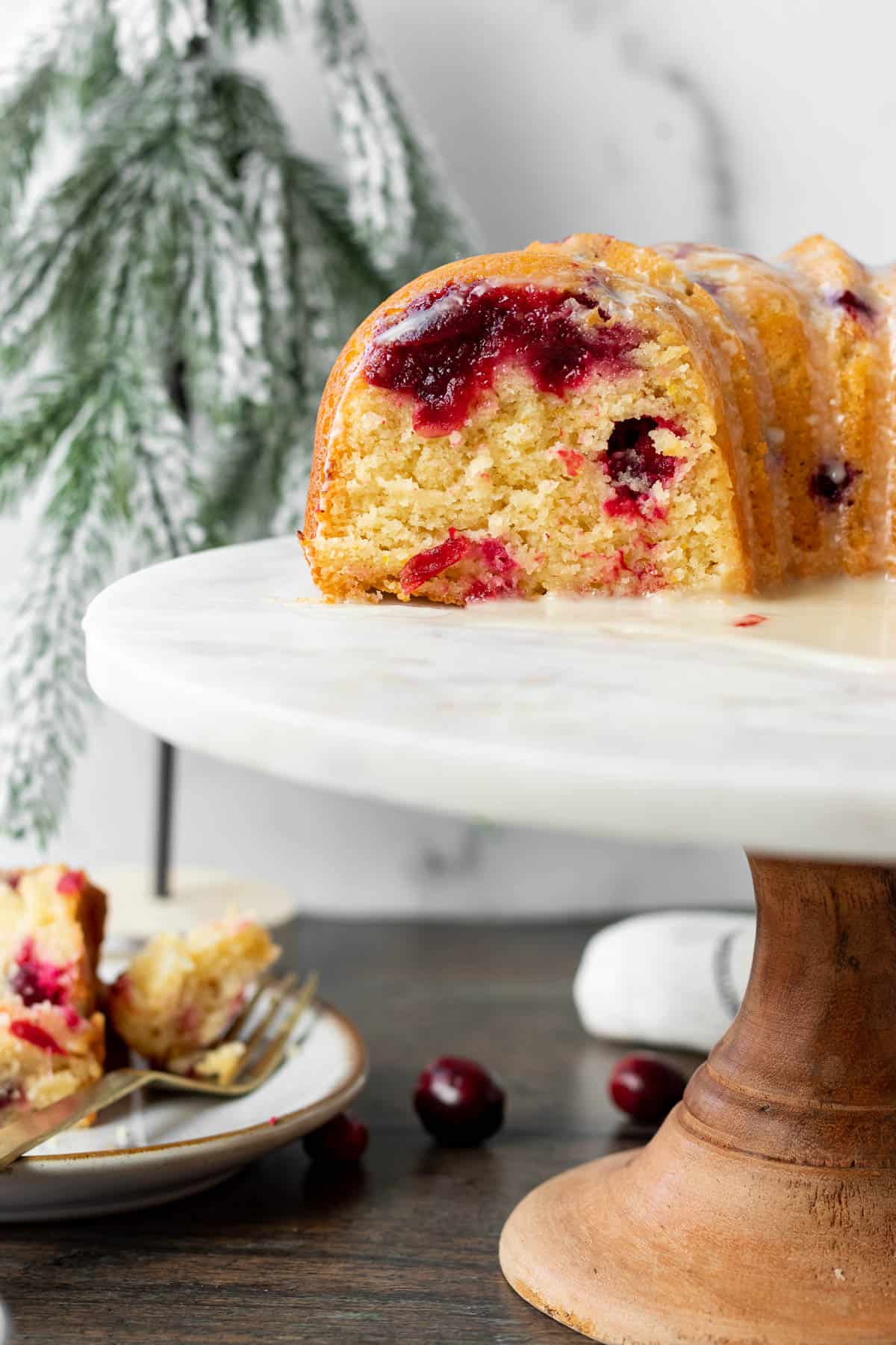 cut cranberry orange bundt cake on a wood and marble cake stand