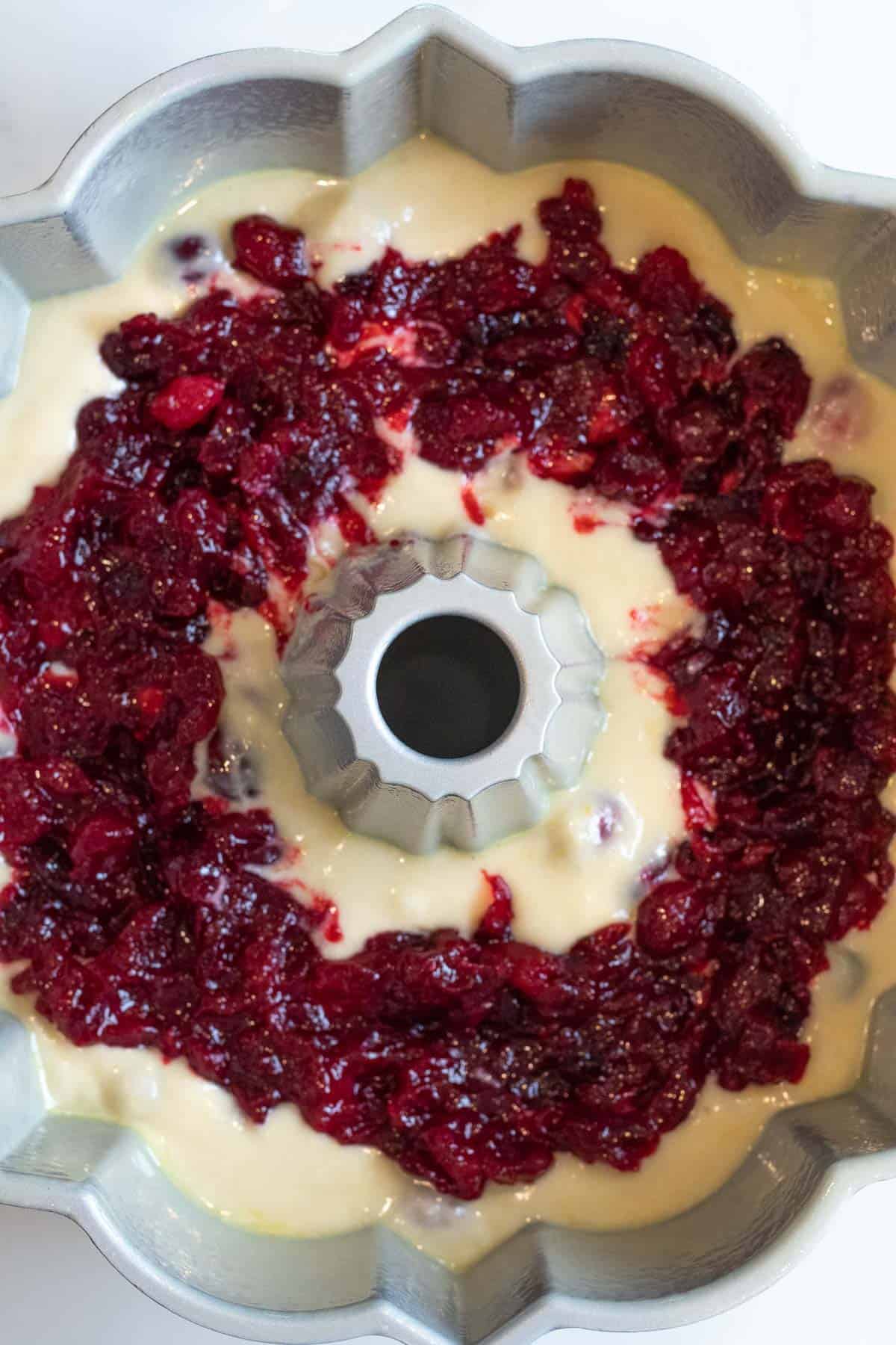 cranberry orange cake batter in a bundt pan layered with cranberry sauce