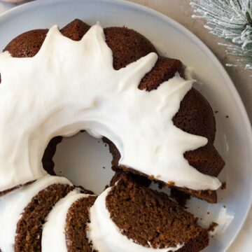 gingerbread bundt cake with a cream cheese glaze on a gray plate sitting on a light brown background