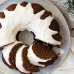 gingerbread bundt cake with a cream cheese glaze on a gray plate sitting on a light brown background
