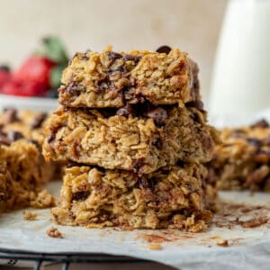 a stack of three chocolate chip baked oatmeal squares with a bowl of berries and carafe of milk in the background