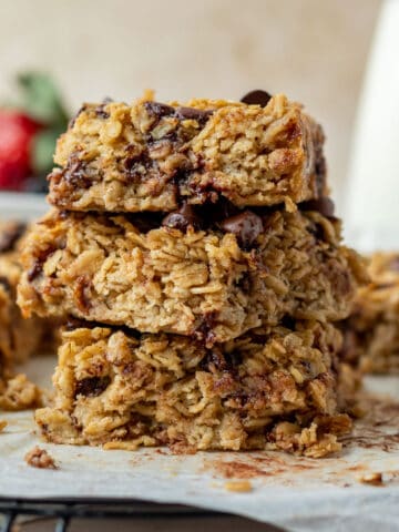 a stack of three chocolate chip baked oatmeal squares with a bowl of berries and carafe of milk in the background