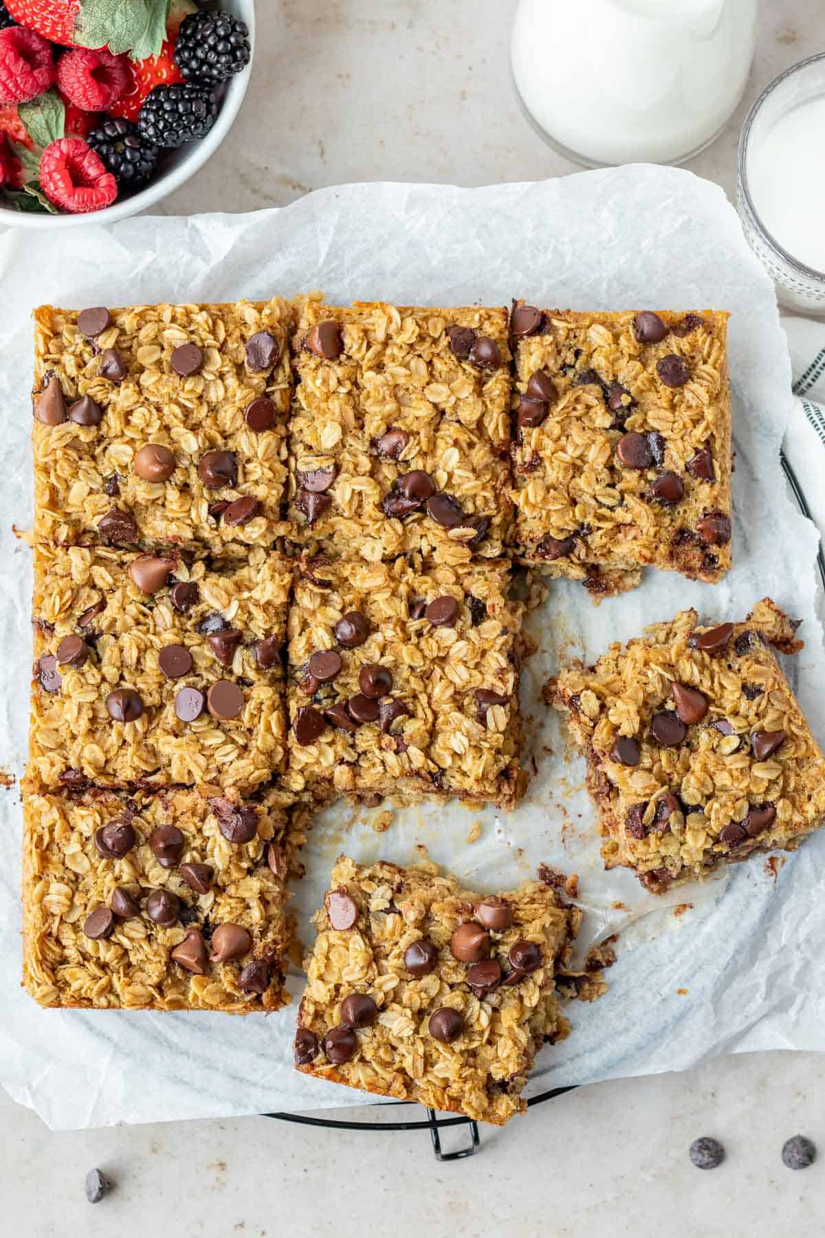 chocolate chip baked oatmeal cut into squares sitting on parchment paper with a bowl of berries in the background