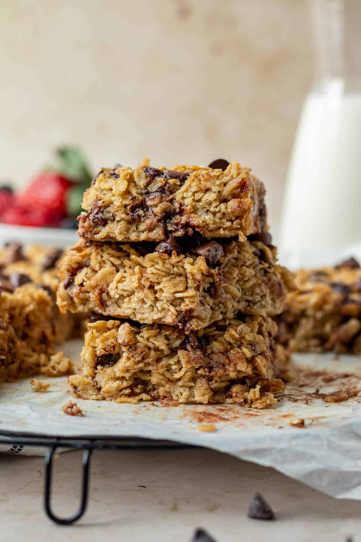 a stack of three chocolate chip baked oatmeal squares with a bowl of berries and carafe of milk in the background