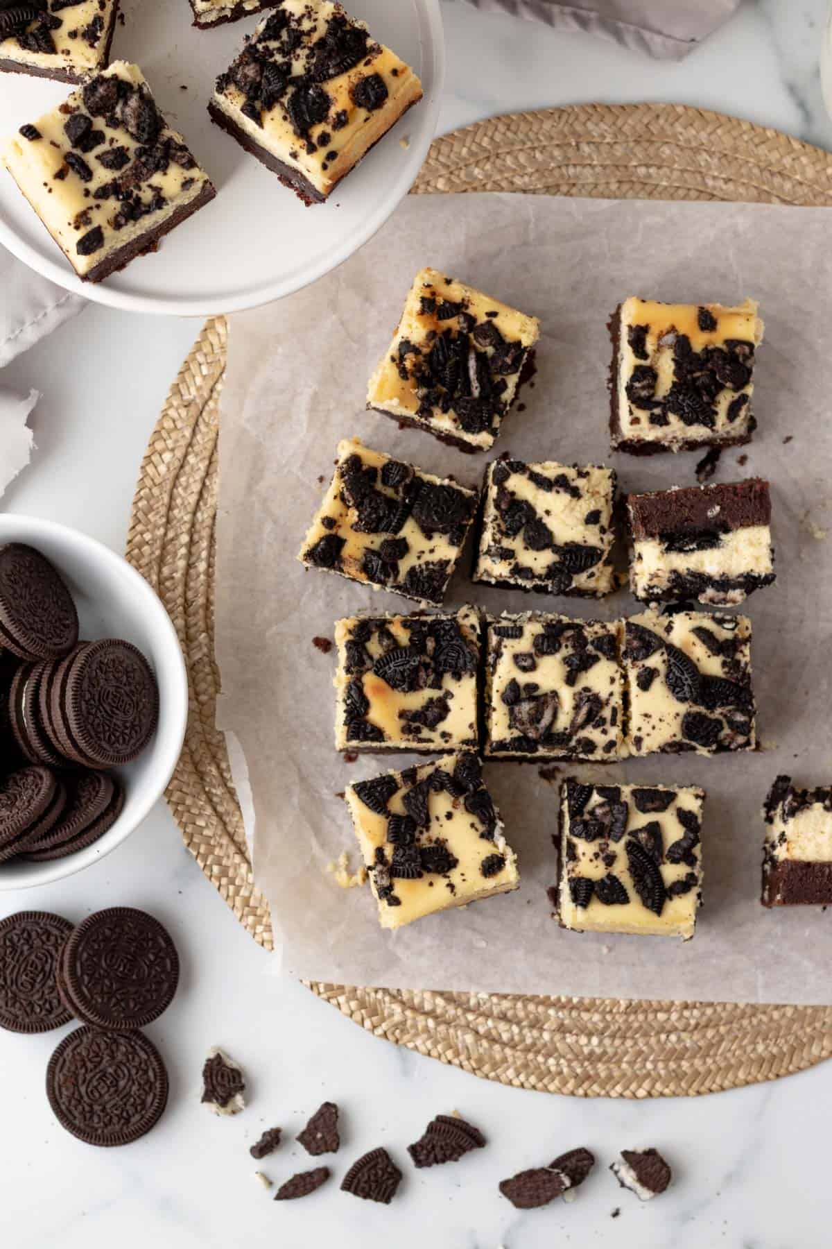 oreo cheesecake bars sliced and sitting on parchment paper with a bowl of oreos next to them