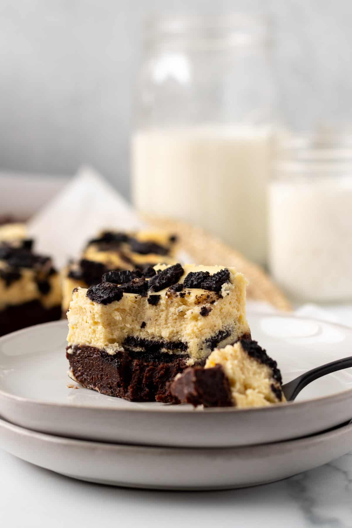 oreo cheesecake bar sitting on a plate with a bite of the bar on a fork and milk in the background