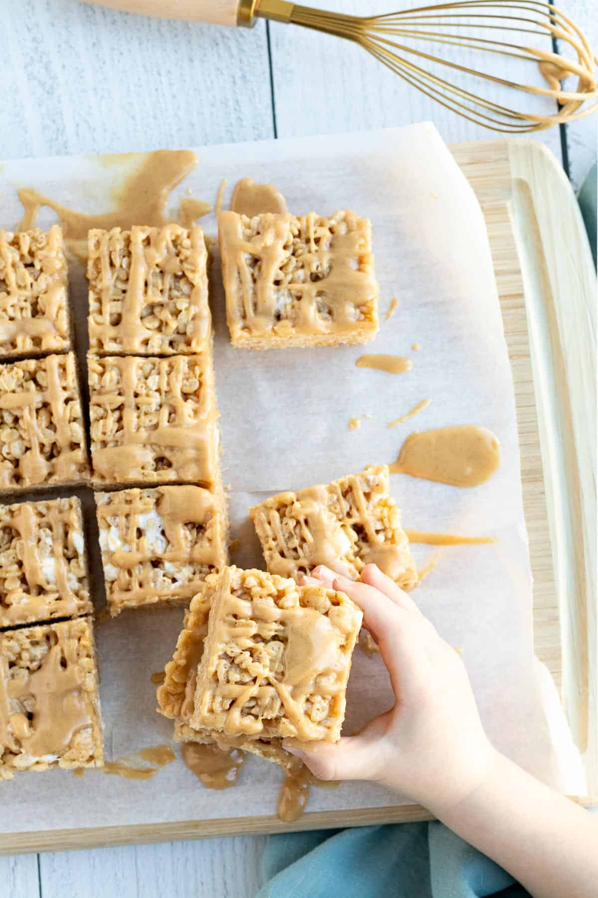 peanut butter rice krispie bars sitting on parchment with a child's hand reaching for a bar