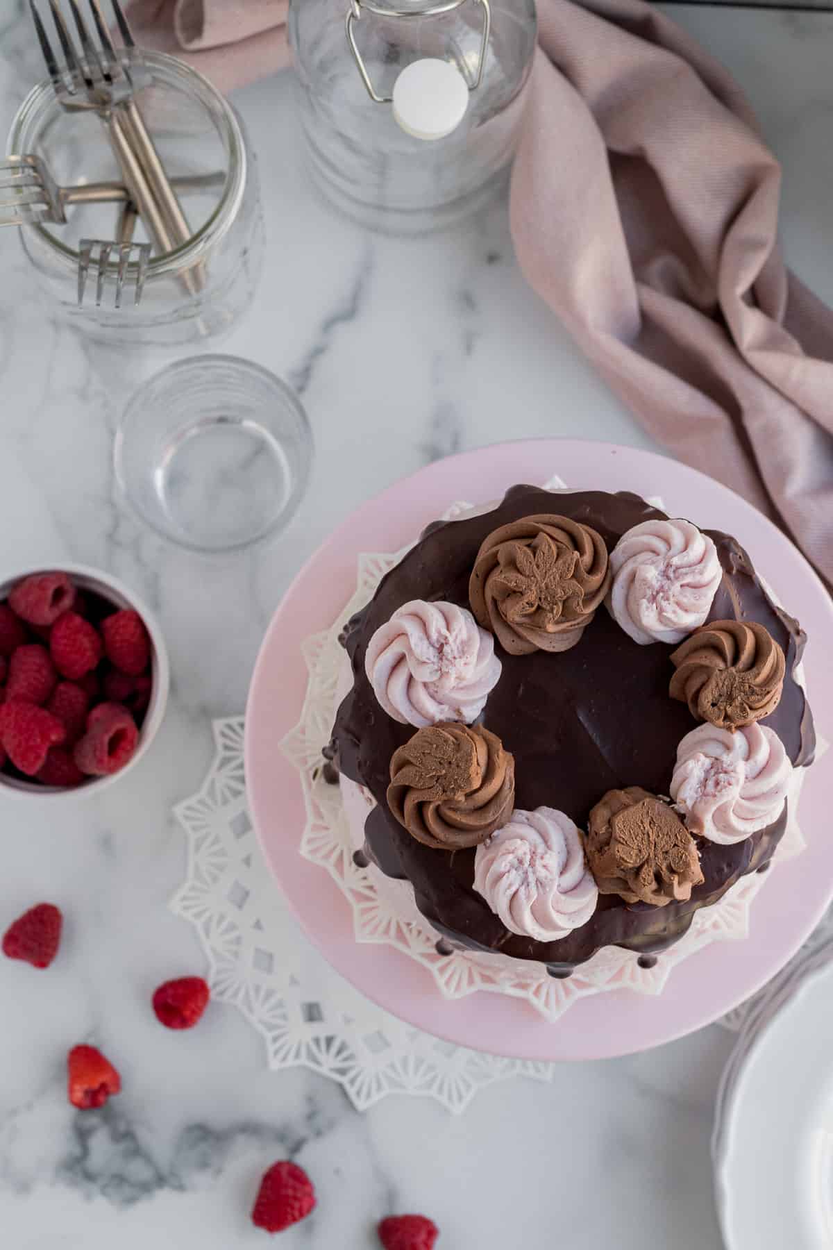 chocolate raspberry cake on a cake stand with raspberries in a bowl sitting next to it