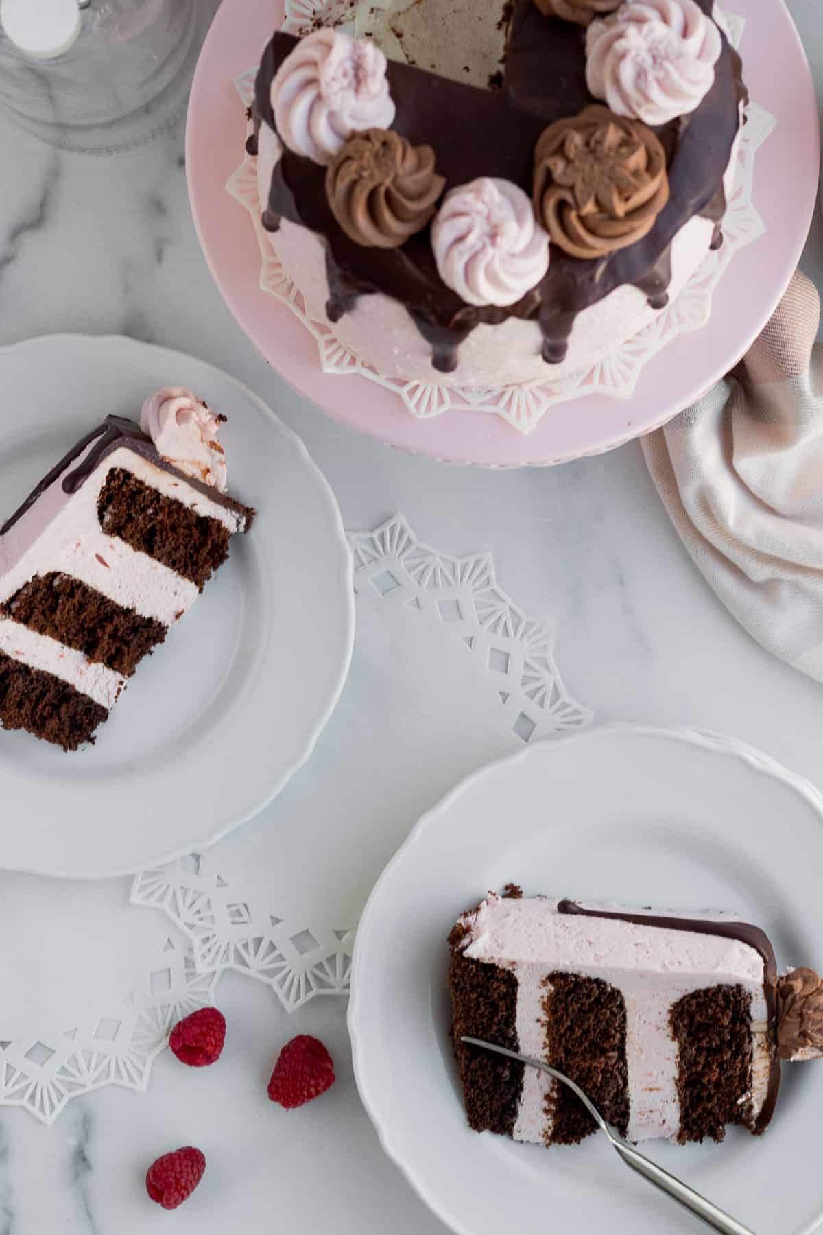 chocolate raspberry cake on a pink cake stand with 2 plates of sliced cake