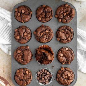 a muffin pan of triple chocolate muffins with one muffin with a bite out of it