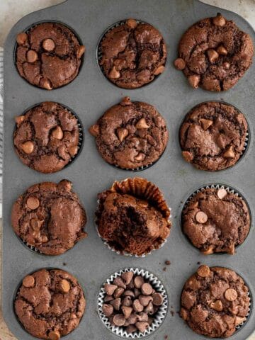 a muffin pan of triple chocolate muffins with one muffin with a bite out of it