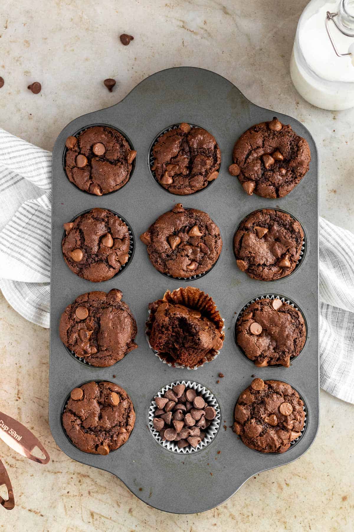 a muffin pan of triple chocolate muffins with one muffin with a bite out of it