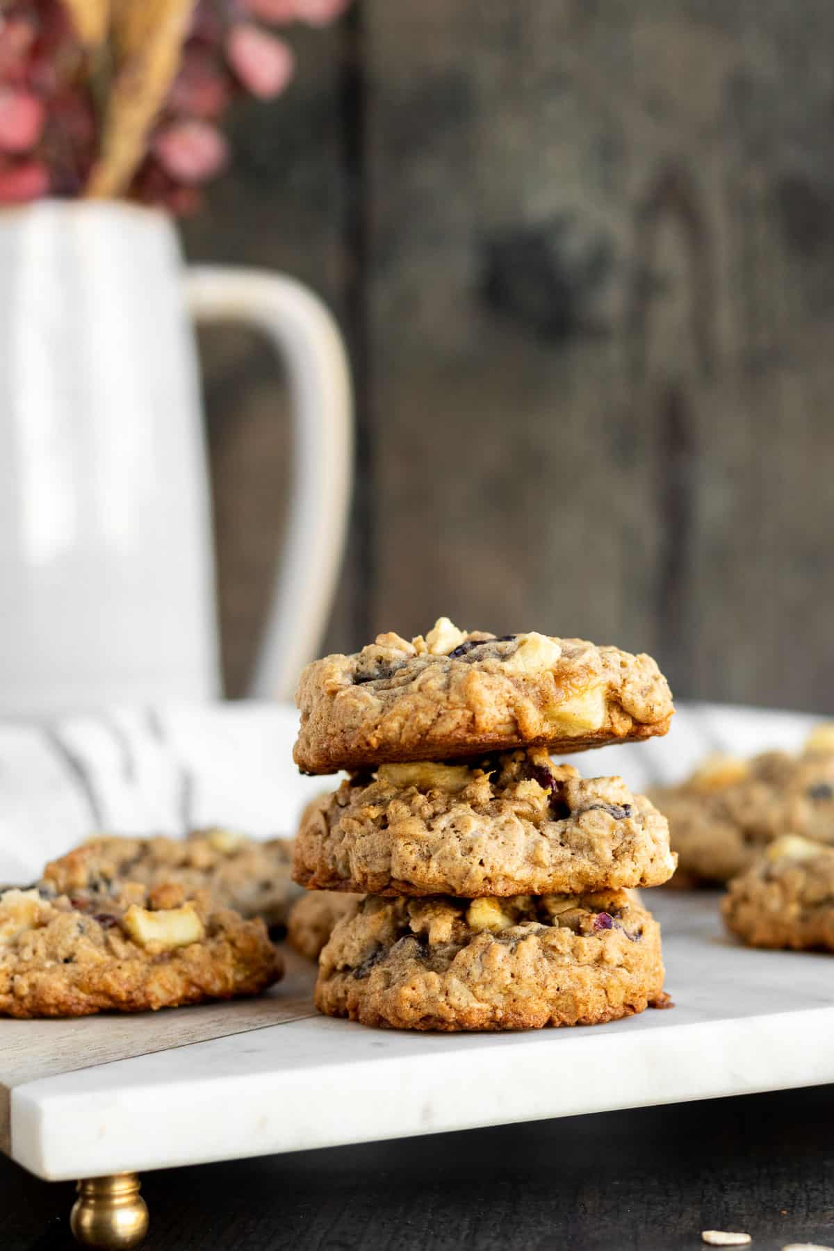 stack of 3 apple oatmeal cookies on a marble board with a kitchen towel and gray pitcher in the background