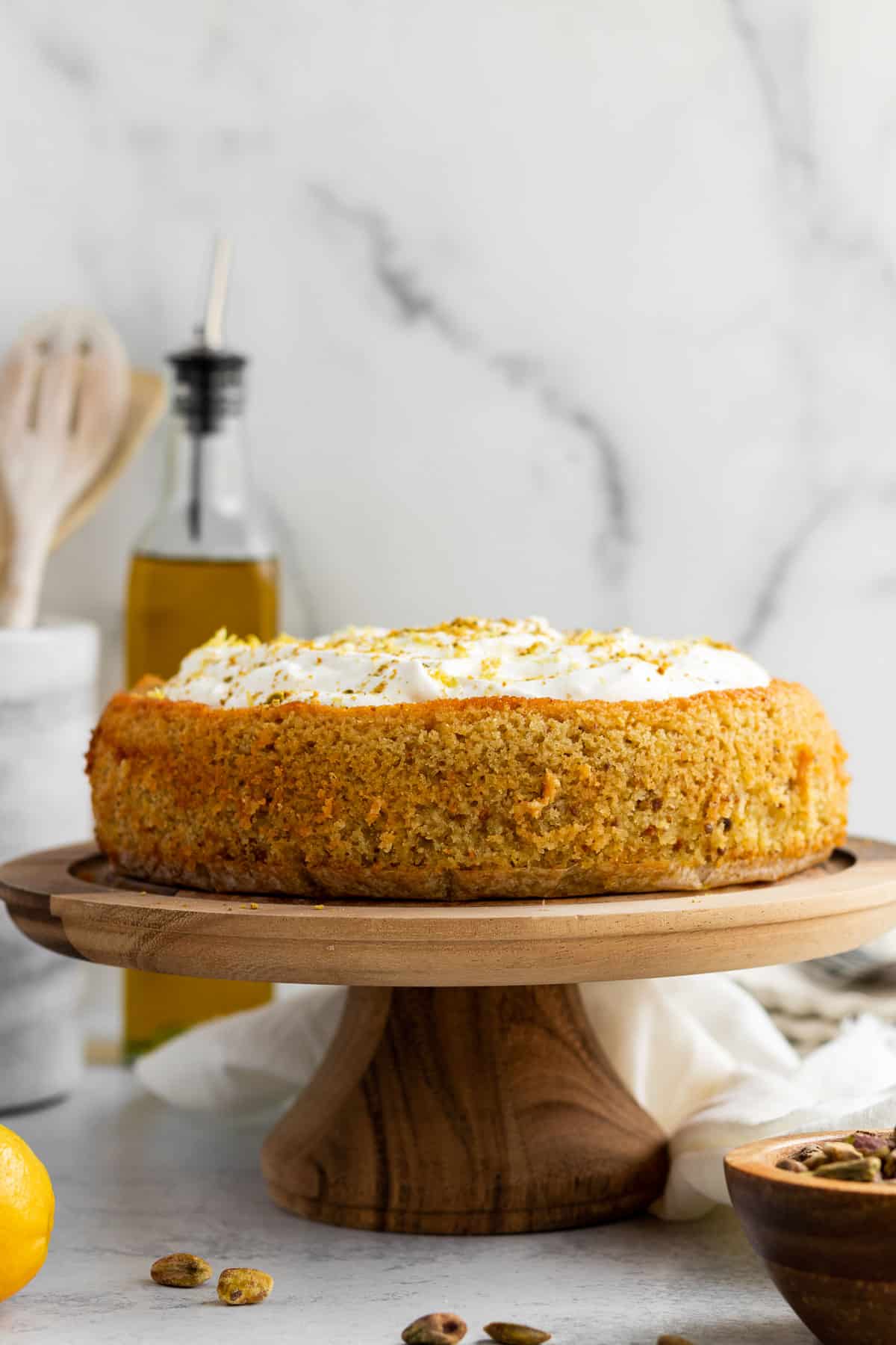 lemon pistachio cake with whipped cream on a wood cake stand