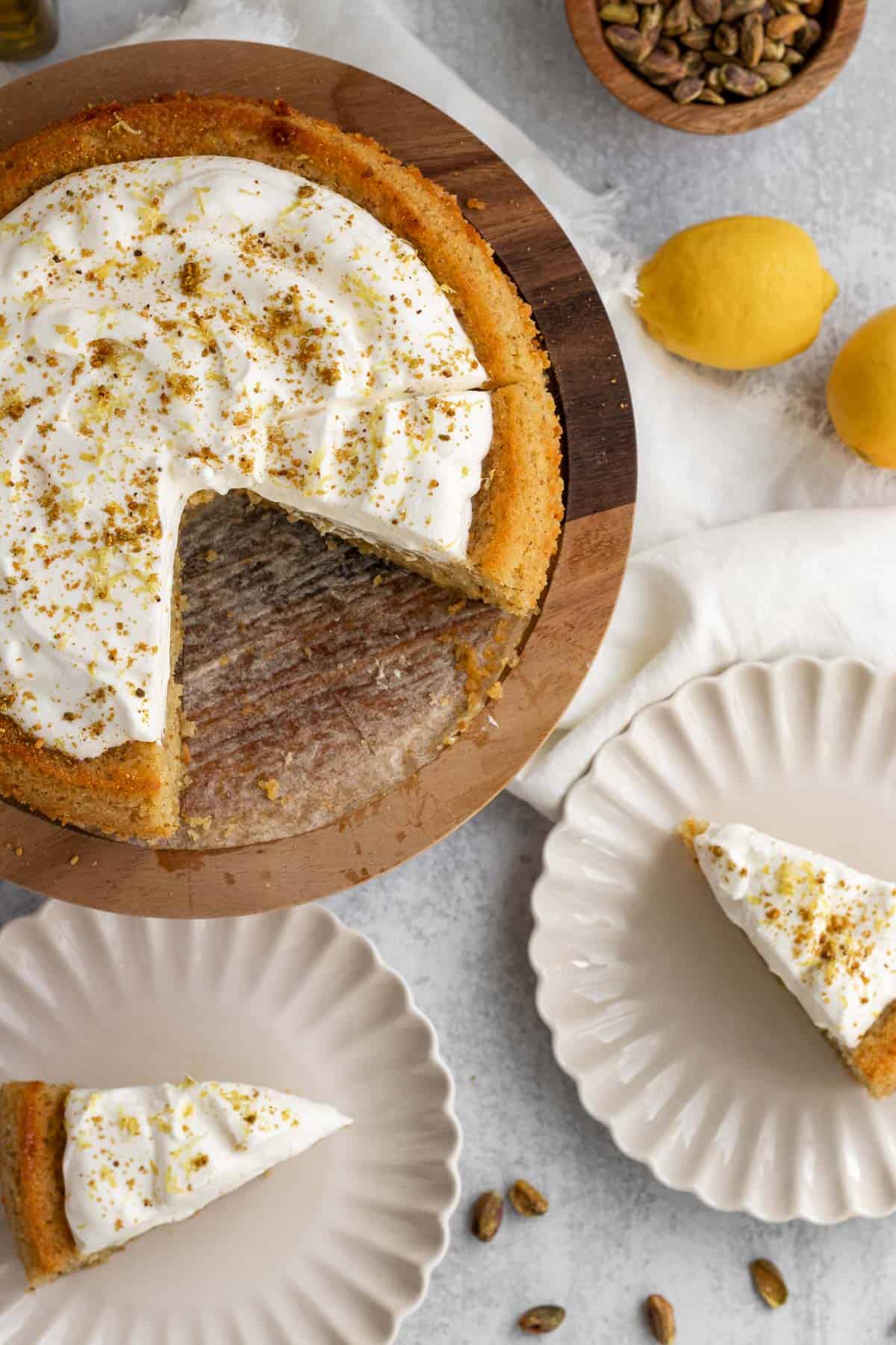 lemon pistachio cake on a wooden cake stand with 2 slices cut and on cream colored plates 