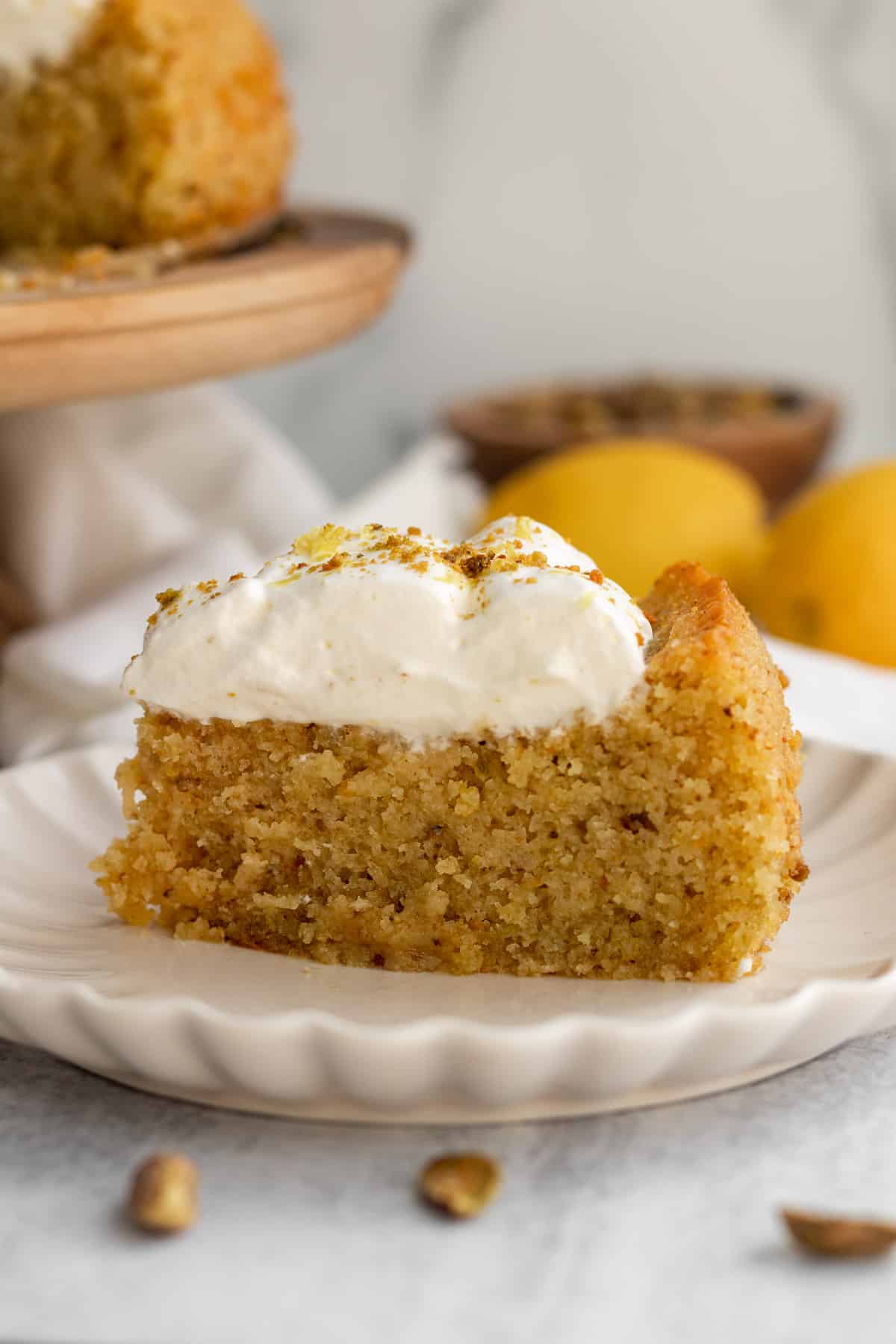 a slice of lemon pistachio cake on a cream scalloped plate