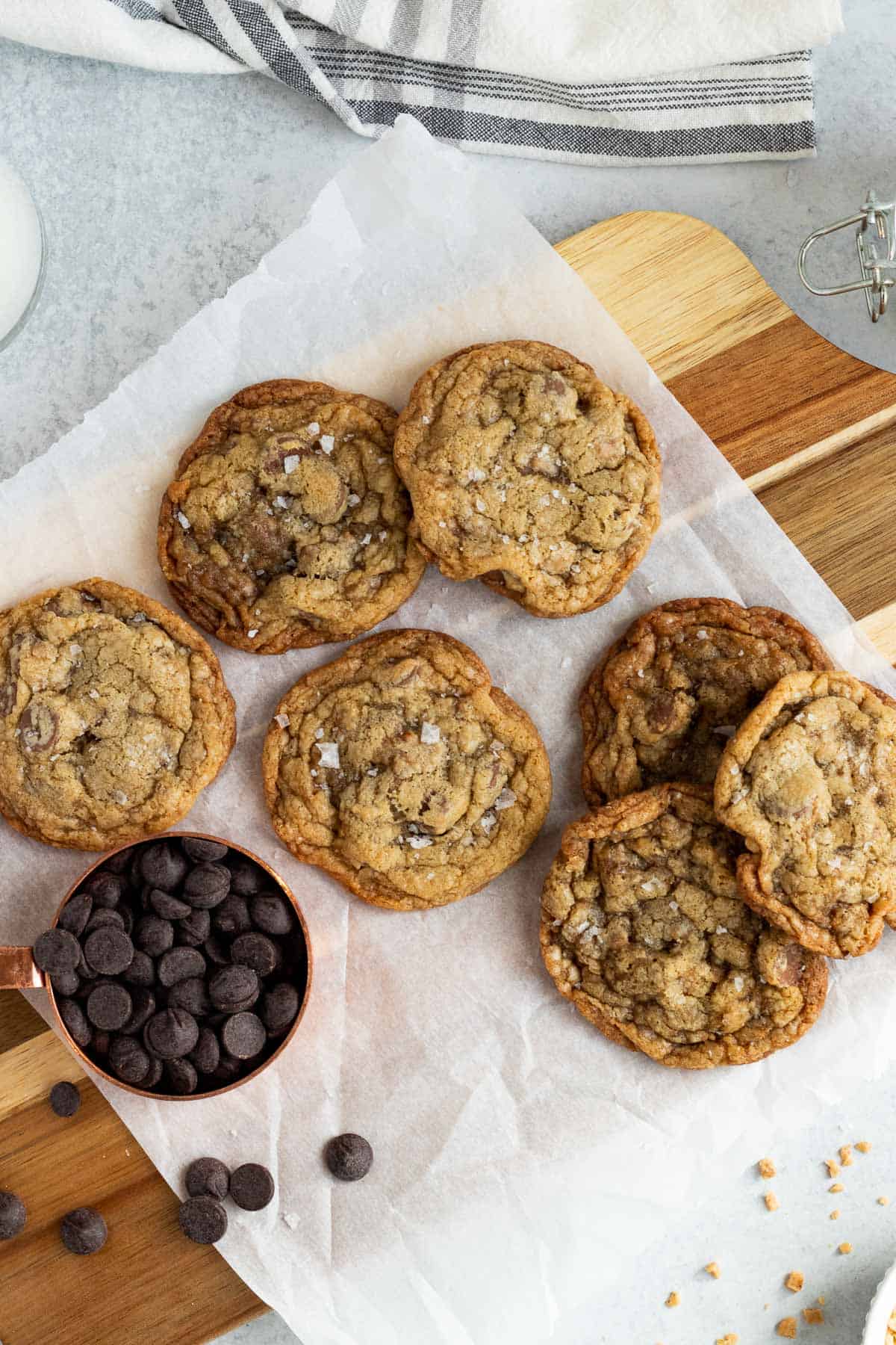 salted toffee chocolate chip cookies on parchment paper with a measuring cup of chocolate chips