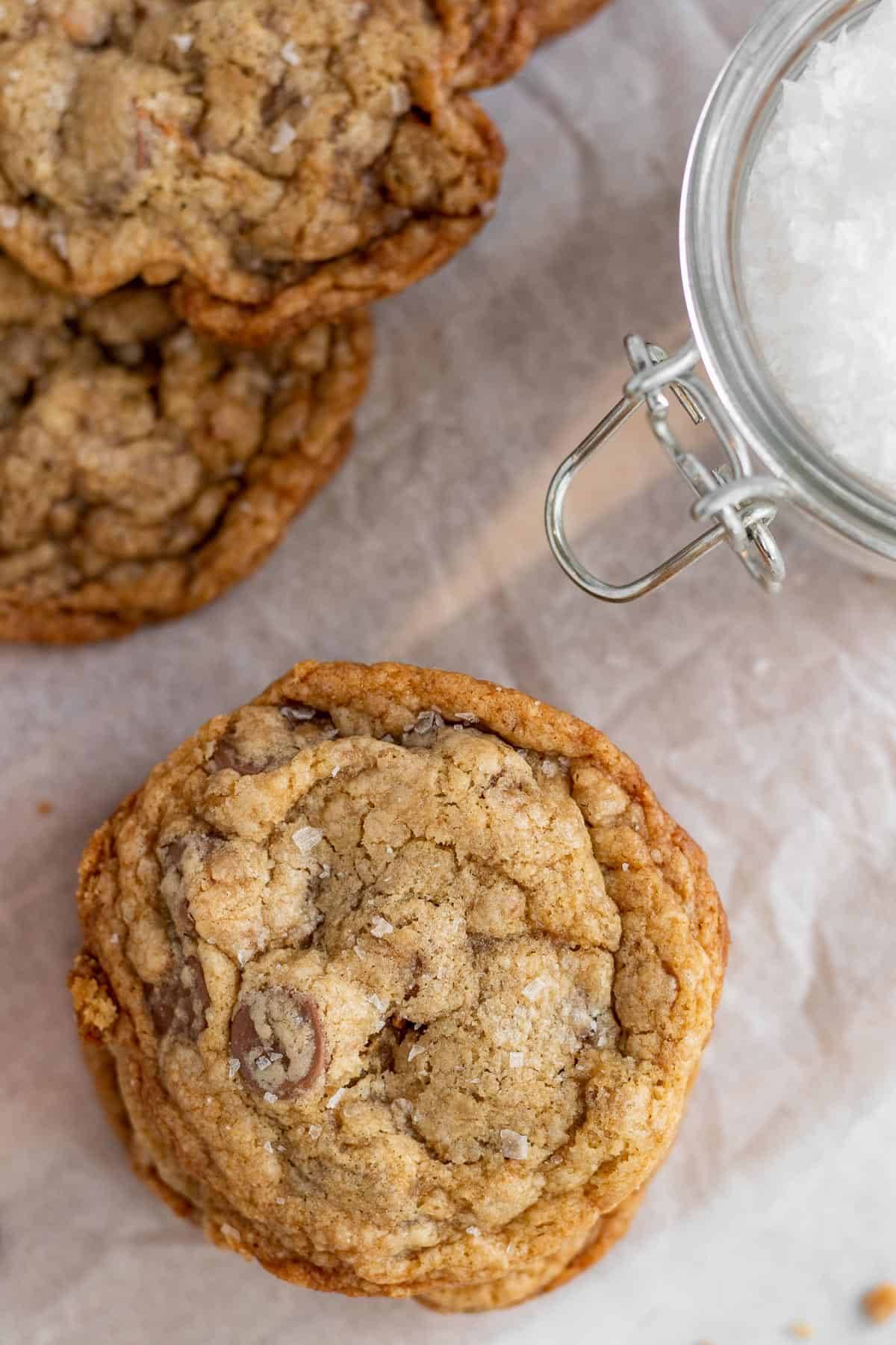 salted toffee chocolate chip cookies on parchment with a glass jar of sea salt