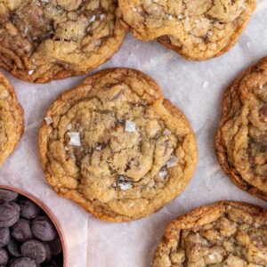 salted toffee chocolate chip cookies in a pile with a measuring cup of chocolate chips