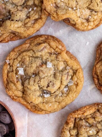 salted toffee chocolate chip cookies in a pile with a measuring cup of chocolate chips