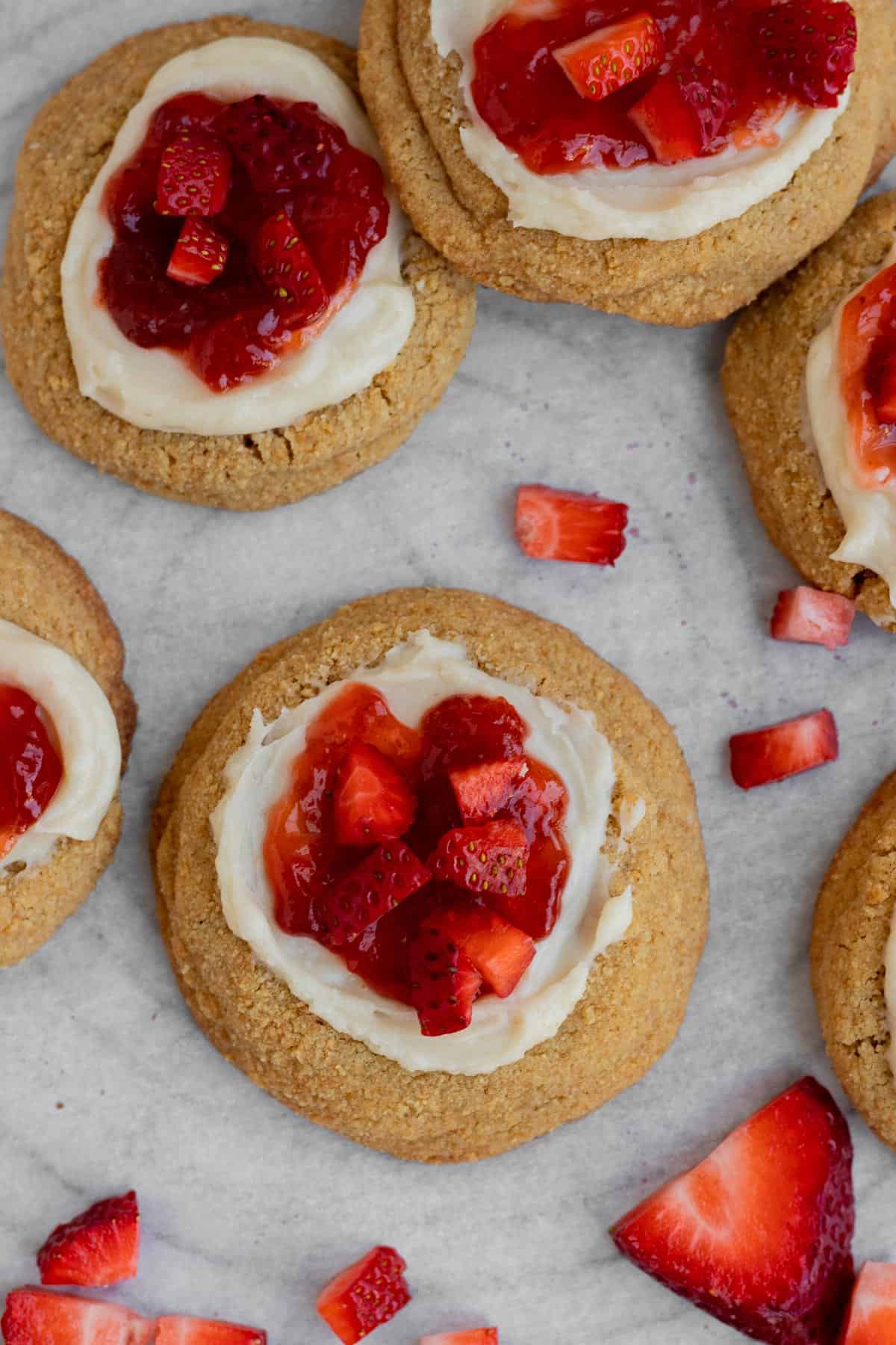 strawberry cheesecake cookies with cheesecake filling and strawberry jam with fresh strawberries sitting on parchment paper